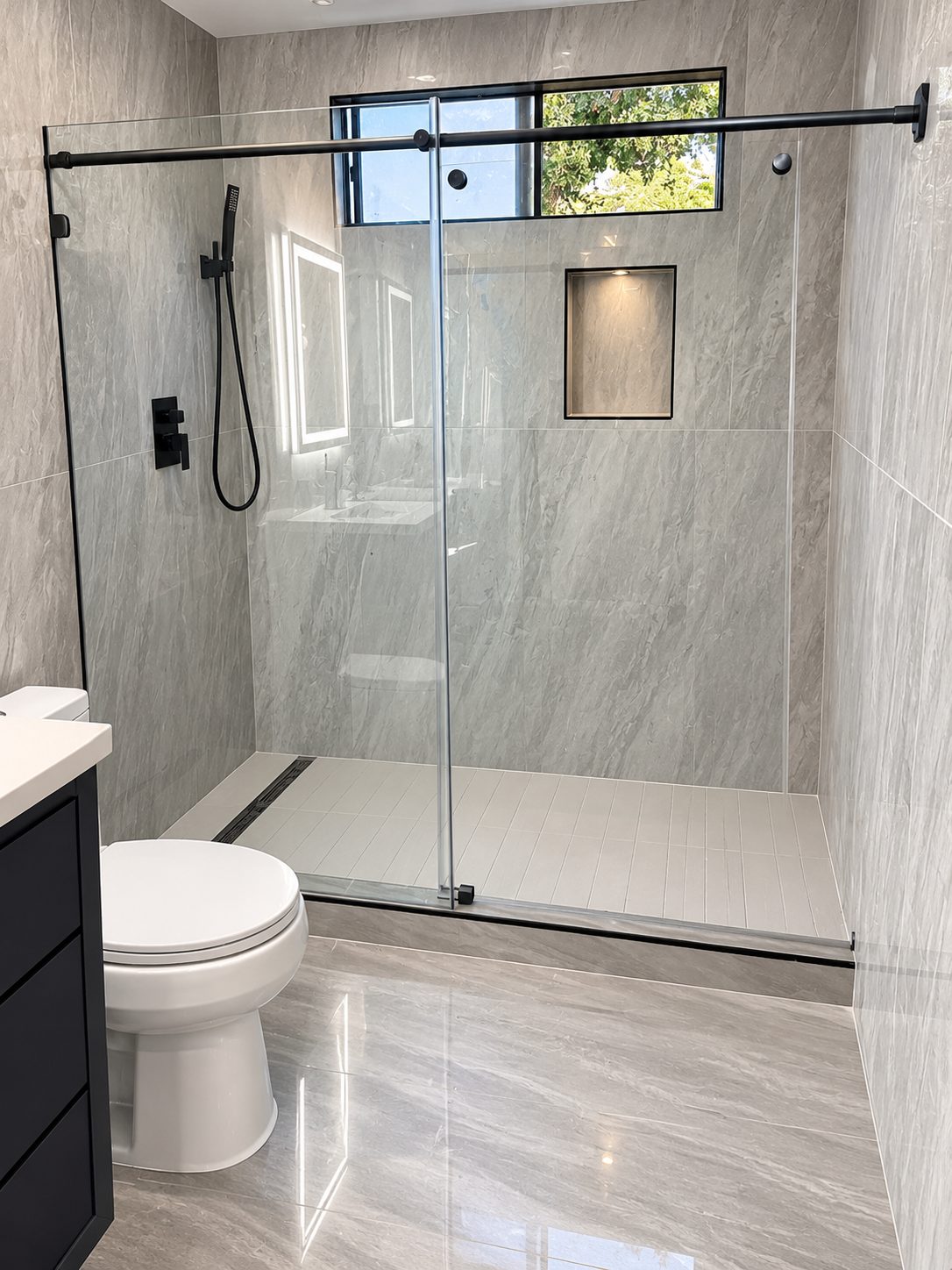 Grey stone shower with matte black fixtures and linear drain
