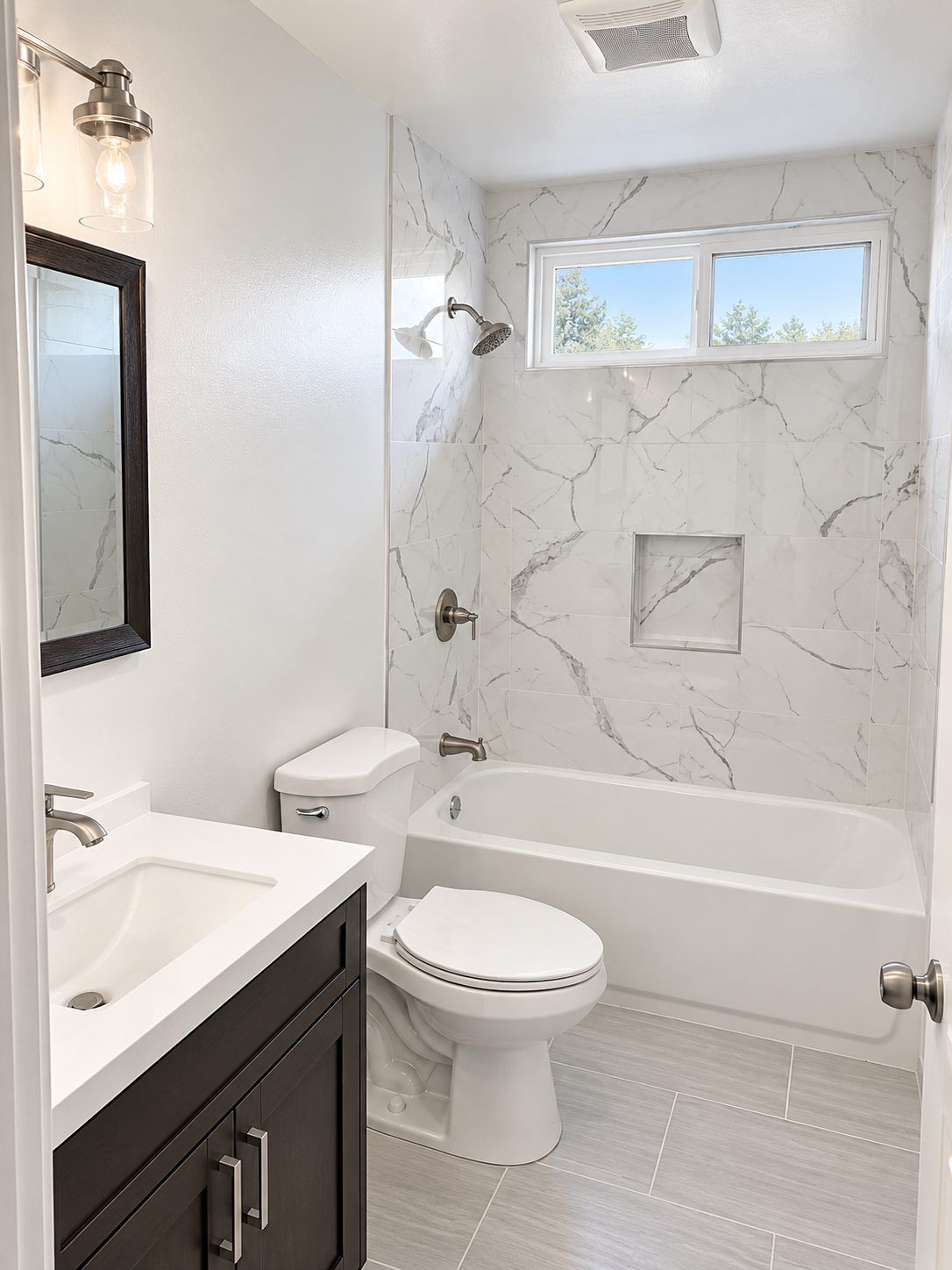 Tub with marble-look tile surround and dark vanity