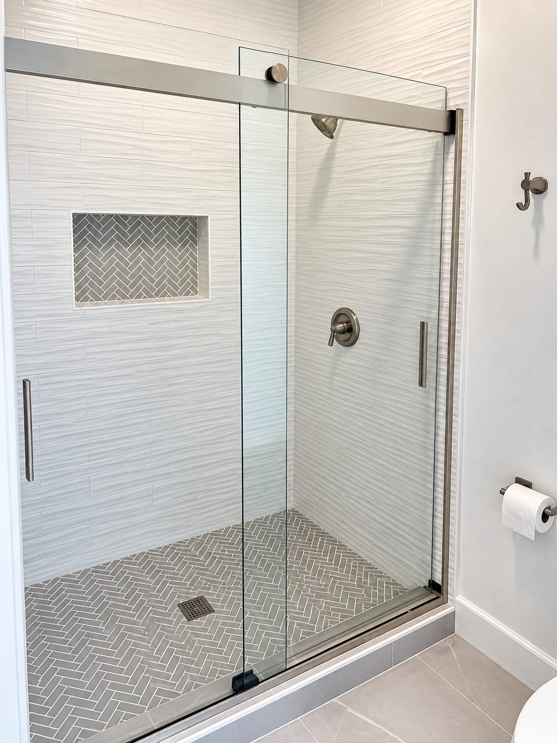 Textured white tile shower with grey herringbone floor