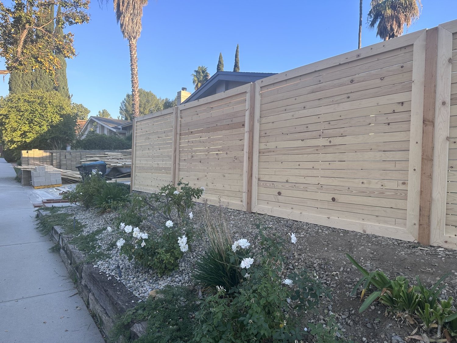 Natural horizontal cedar fence along the sidewalk with a flower bed