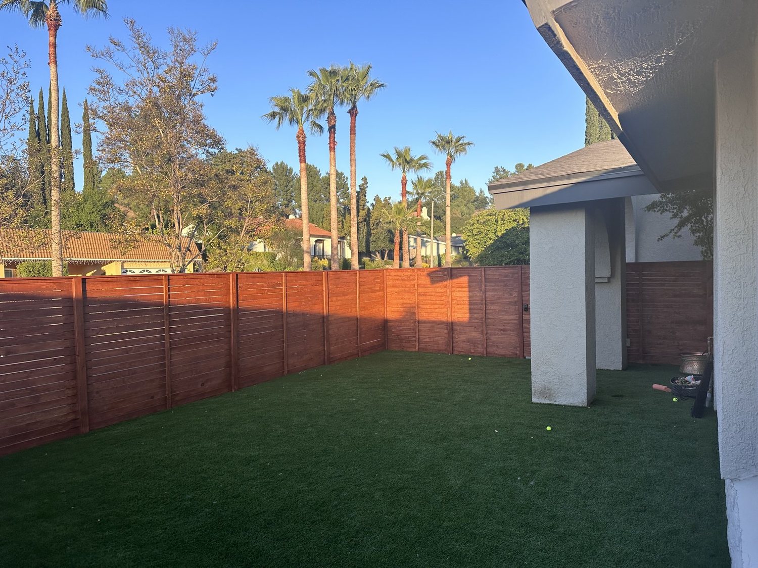 Stained horizontal redwood fence around a green lawn